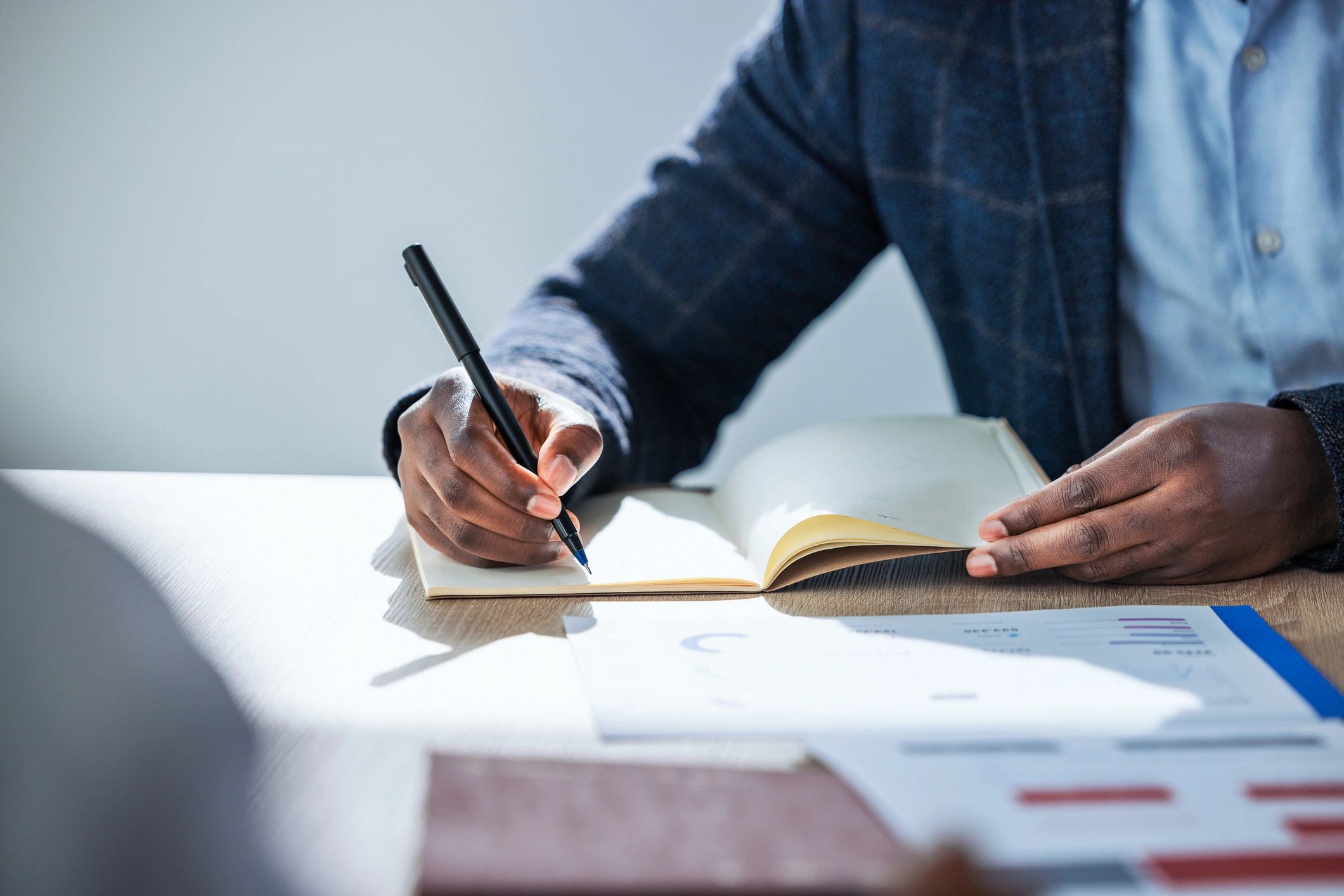 Person writing notes at desk with documents